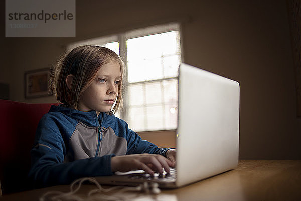 Junge benutzt Laptop-Computer  während er am Tisch sitzt