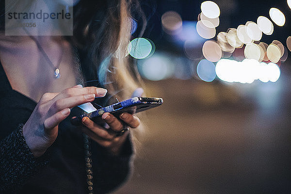Ein Teil der Frau benutzt ein Smartphone  während sie nachts im Freien steht