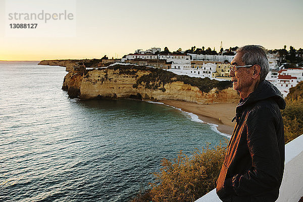 Seitenansicht eines nachdenklichen älteren Mannes mit Blick auf das Meer bei der Stadt
