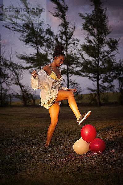 Seitenansicht eines glücklichen Teenagers  der in der Abenddämmerung Ballons auf dem Feld platzen lässt