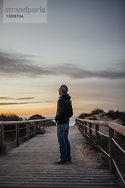 Älterer Mann in voller Länge steht bei Sonnenuntergang am Strand gegen den Himmel