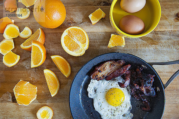 Draufsicht auf Orangen mit Eiern und Speck auf Holztisch