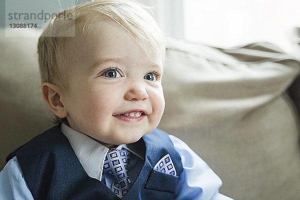 Nahaufnahme eines süßen  lächelnden Babyjungen im Anzug  der zu Ostern auf dem heimischen Sofa wegschaut