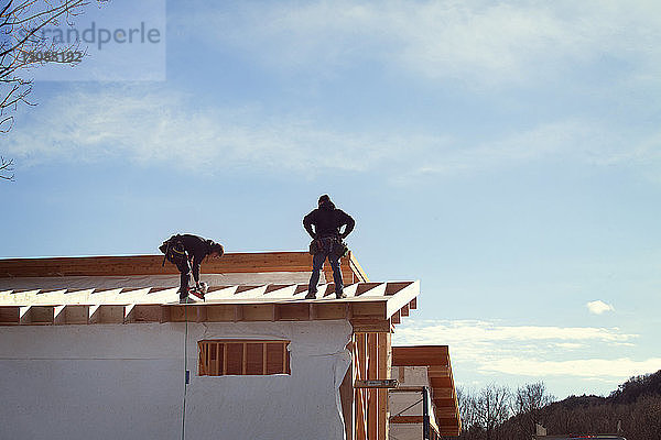 Arbeiter beim Bau von Hausdächern gegen den Himmel während eines sonnigen Tages