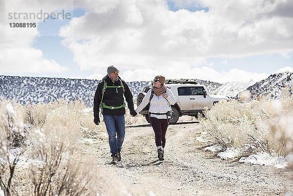 Paar in voller Länge an den Händen haltend beim Spaziergang in der Wüste vor bewölktem Himmel im Winter