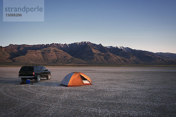 Zelt und Auto auf trockenem Feld gegen Berge und Himmel in der Alvord-Wüste