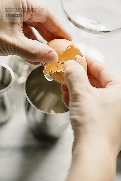 Beschnittenes Bild einer Frau  die ein Ei in einem Trinkglas zerbricht