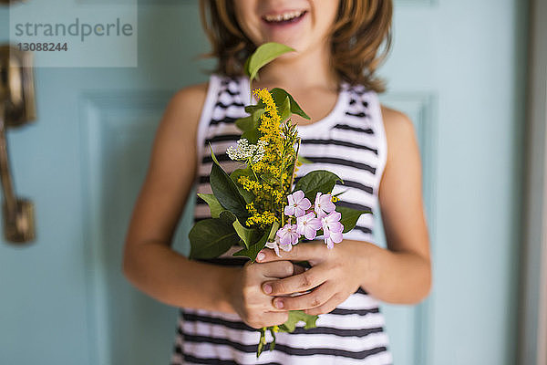 Mittendrin ein Mädchen  das Blumen und Blätter hält  während es vor der Tür steht