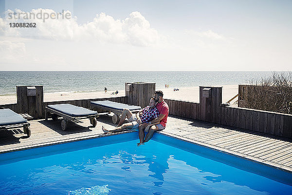 Romantisches homosexuelles Paar  das sich am Pool neben Liegestühlen gegen den Himmel ausruht