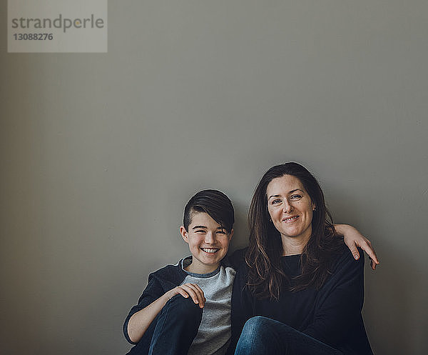 Porträt einer glücklichen Mutter mit Sohn  die zu Hause an der Wand sitzt
