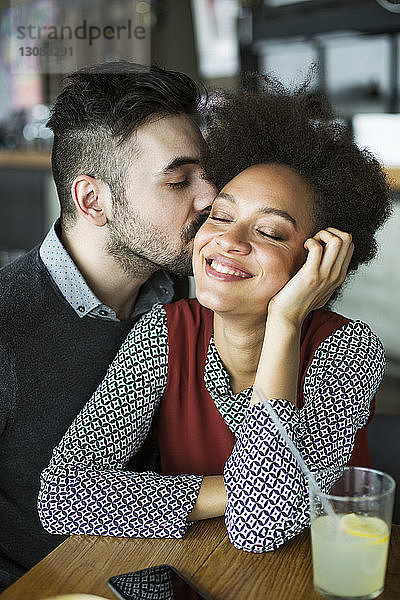 Mann küsst glückliche Frau  die im Restaurant sitzt