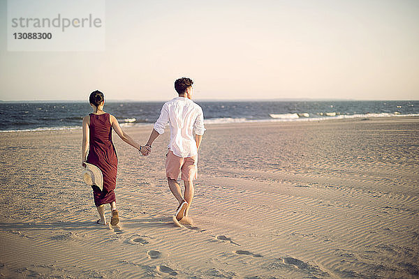 Rückansicht eines Paares  das sich beim Spaziergang am Strand im Sand an den Händen hält