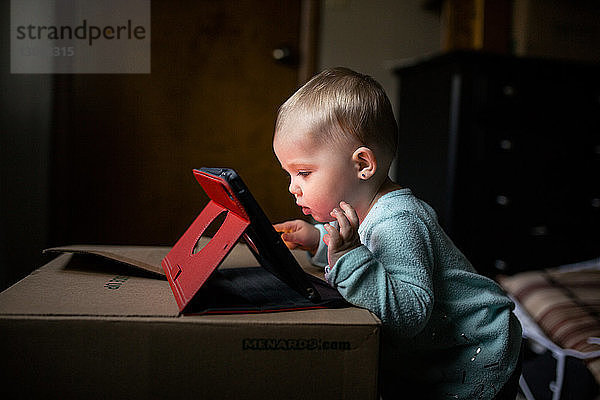 Seitenansicht eines kleinen Mädchens  das einen Tablet-Computer benutzt  während es zu Hause an der Box steht