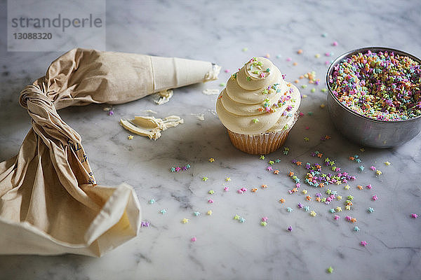 Draufsicht auf den Zuckergussbeutel von Cupcake und Streusel auf der Küchentheke