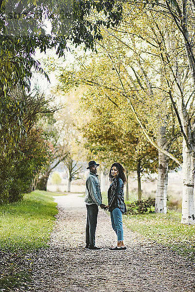Porträt eines Paares  das sich im Herbst auf einem Fußweg im Park an den Händen hält