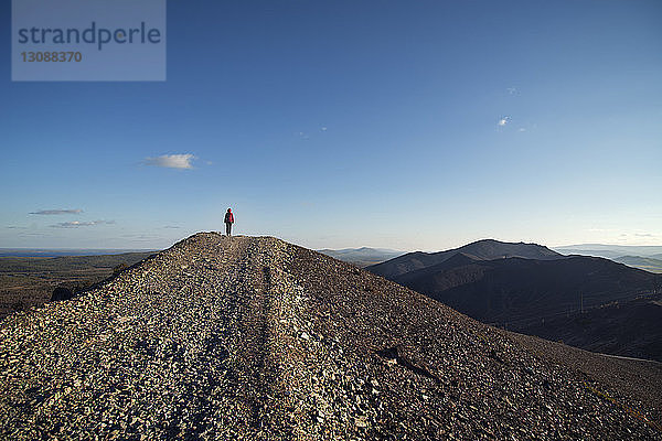 Fernansicht eines Wanderers  der auf einem Berg vor blauem Himmel steht