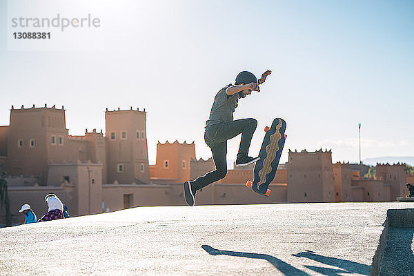 Seitenansicht eines Mannes  der an einem sonnigen Tag einen Stunt auf einem Skateboard vor einem Schloss vorführt