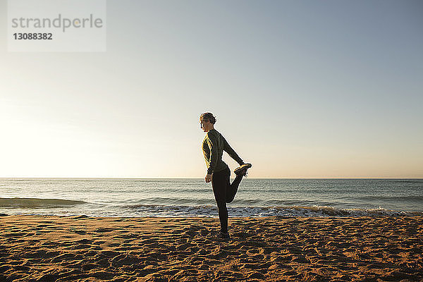 Frau in voller Länge beim Yoga am Strand bei klarem Himmel