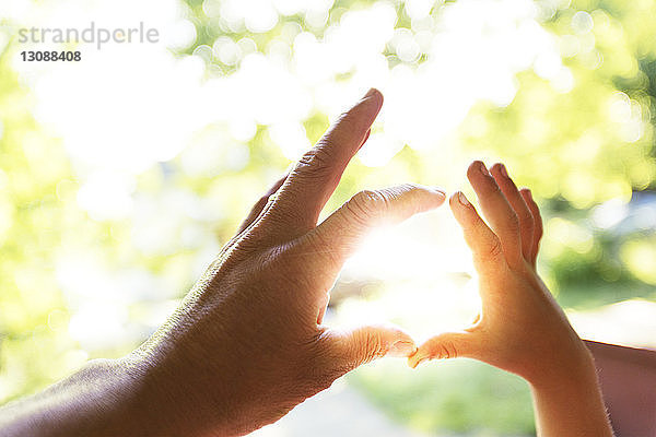 Vater und Kind machen berührende Hände gegen das Sonnenlicht