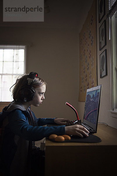 Seitenansicht eines Jungen  der zu Hause am Laptop sitzt