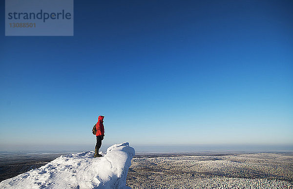 Wanderer steht auf schneebedecktem Berg vor strahlend blauem Himmel