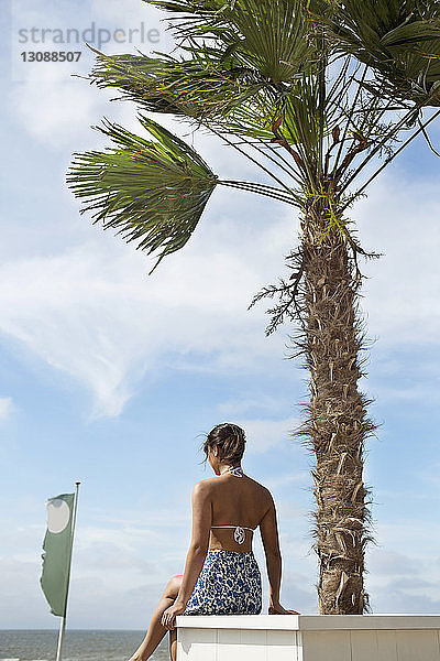 Rückansicht einer Frau  die auf einem Sitz am Strand gegen den Himmel sitzt