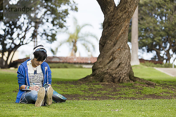 Teenager-Mädchen schreibt auf Tagebuch  während sie im Park Musik hört