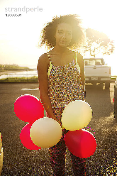 Porträt eines jungen Mädchens  das mit Luftballons auf einem Feld an einem sonnigen Tag steht