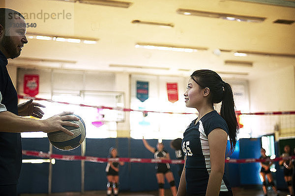 Männlicher Trainer hält Ball und spricht auf dem Volleyballfeld über Mädchen