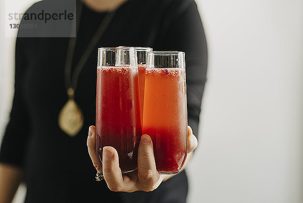 Mittelteil einer Frau  die einen Cocktail hält  während sie zu Hause an der Wand steht