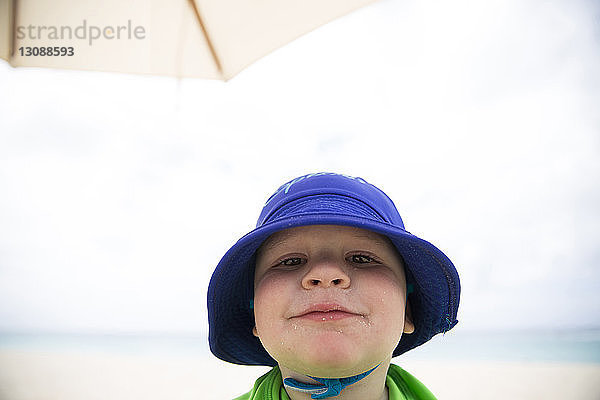 Nahaufnahme eines Jungen mit Hut  der am Strand gegen den Himmel steht
