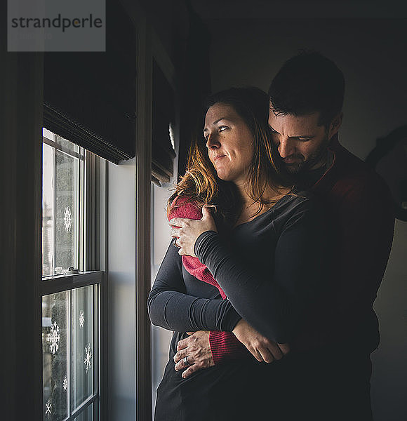 Paar  das sich umarmt  während es zu Hause am Fenster steht