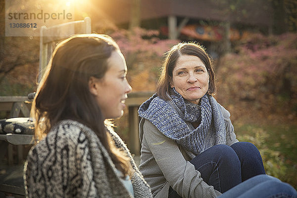 Tochter und Mutter unterhalten sich  während sie gegen ein Blockhaus im Wald sitzen