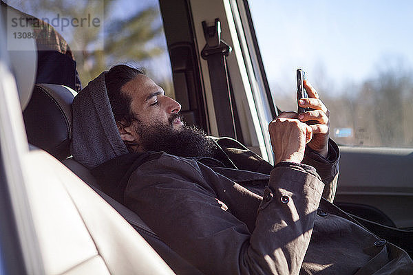 Seitenansicht eines Mannes  der ein Smartphone benutzt  während er im Auto sitzt