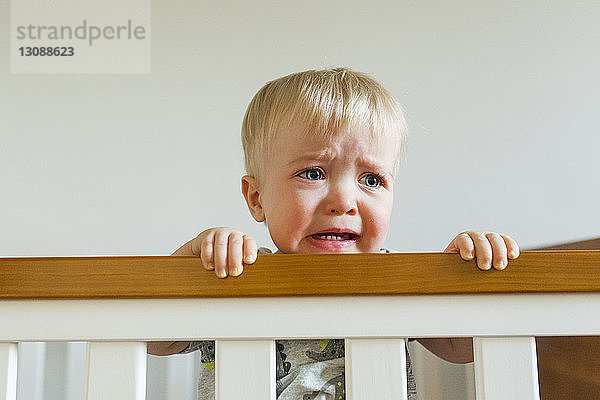 Süßer kleiner Junge schaut weg  während er zu Hause in der Krippe weint