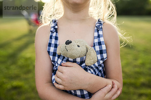 Mittendrin ein Mädchen  das ein Stofftier in einem Kleid auf einem Feld im Hinterhof hält
