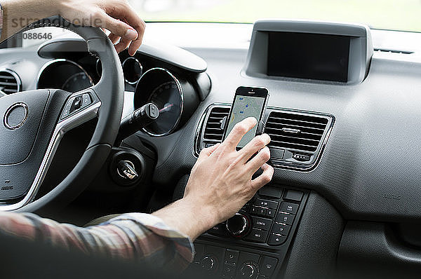 Ausgeschnittenes Bild eines Mannes  der GPS auf einem Smartphone im Auto benutzt
