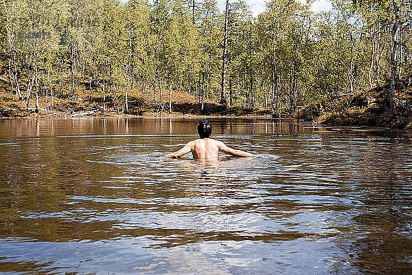 Rückansicht eines Mannes ohne Hemd  der im See im Wald schwimmt