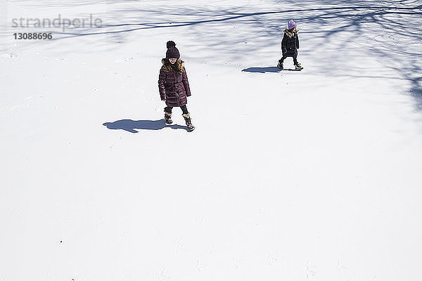 Hochwinkelansicht von Schwestern  die auf einem schneebedeckten Feld gehen