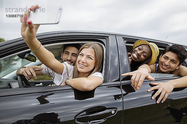 Glückliche männliche und weibliche Freunde  die sich beim Sitzen im Auto Selbsthilfe leisten