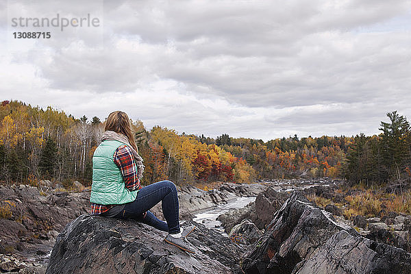 Frau sitzt auf einem Felsen im Jay Cooke State Park vor bewölktem Himmel