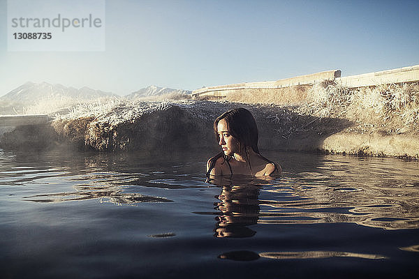 Nachdenkliche Frau entspannt sich in Mammoth Lake Hot Springs gegen den Himmel