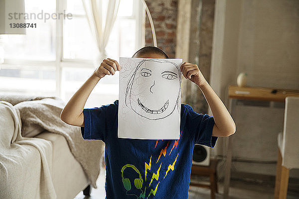 Junge zeigt Zeichnung  während er zu Hause im Wohnzimmer steht