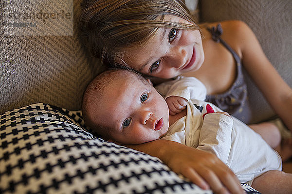 Porträt eines Mädchens mit Baby zu Hause auf dem Sofa liegend