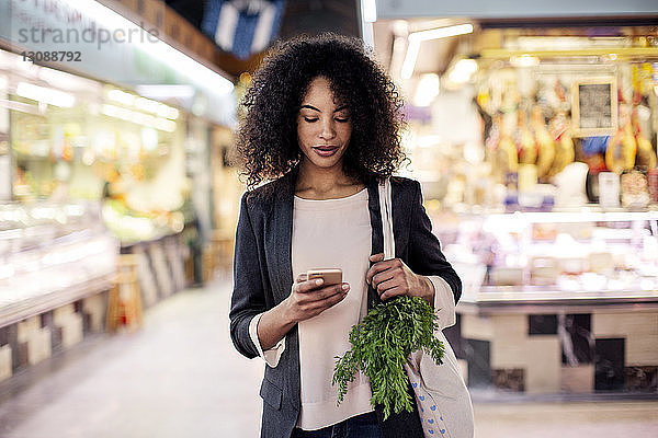 Frau benutzt Mobiltelefon beim Einkaufen auf dem Markt