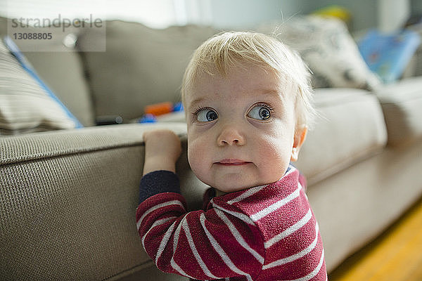 Nahaufnahme eines süßen kleinen Jungen  der wegschaut  während er zu Hause am Sofa sitzt