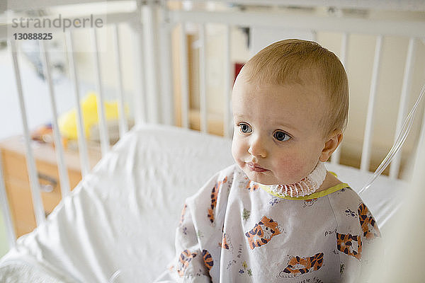 Süßer kranker Junge sitzt in Krankenhauskrippe