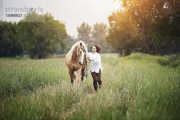 Mittlere erwachsene Frau und Pferd rennen auf Grasfeld auf dem Land