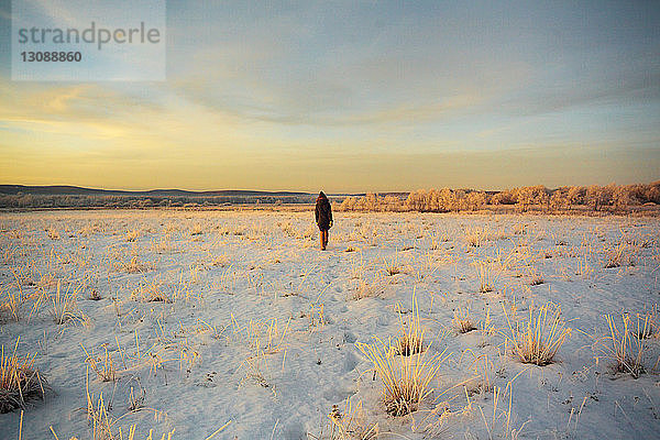 Rückansicht einer Frau  die bei Sonnenuntergang auf einem verschneiten Feld gegen den Himmel läuft