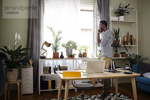 Seitenansicht eines Mannes  der ein Smartphone im Heimbüro benutzt